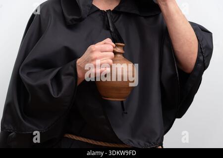 Hands of monk in black robe holding clay jug isolated on white background studio Stock Photo