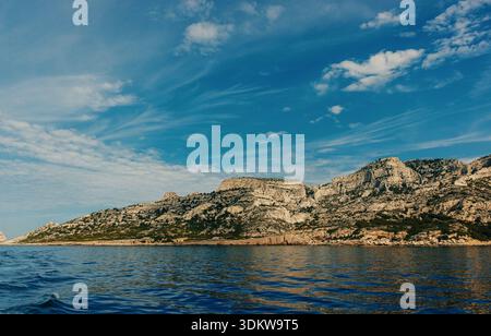 Sunlit Calanques cliffs stretching along the Mediterranean coast with reflections on the calm blue sea. Stock Photo