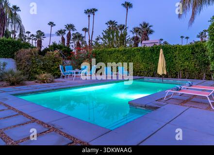 Swimming pool residential backyard with colorful chaise lounge chairs evening night in Palm Springs, California Stock Photo