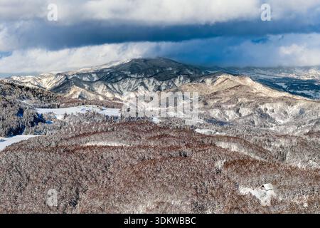 Dramatic clouds hovering over snow-covered mountains and dense forests in Madarao, Nagano Stock Photo