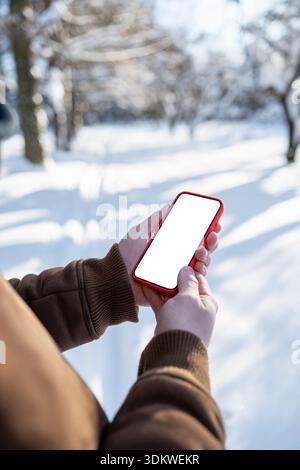 Young man using smartphone and standing outdoors in snowy park during walk. Winter season. Cold weather. Stock Photo