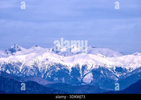 Snow-Capped Mountain Range Under Clear Blue Sky With Clouds and Rolling Foregrounds Stock Photo