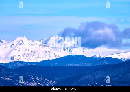 Snow-Capped Mountain Range Under Clear Blue Sky With Clouds and Rolling Foregrounds Stock Photo