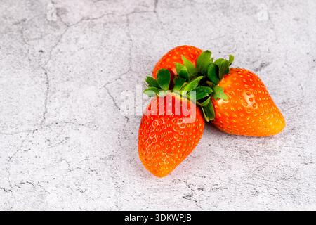 Three ripe strawberries on a light stone background. Minimal healthy snack concept with copy space for text. Stock Photo