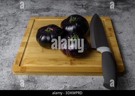 Purple heirloom tomatoes with a chef knife on a wooden cutting board, dark rustic kitchen scene. Healthy food prep for spring cooking. Stock Photo