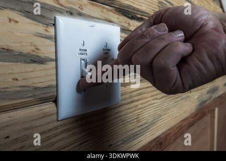 A detailed, side-angle shot of a hand turning on a dual-toggle light switch. The setting features beautiful, natural wood grain paneling, giving the i Stock Photo