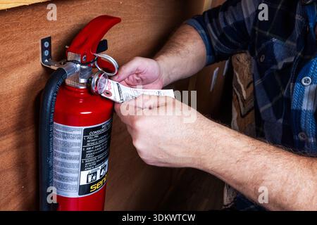 PROSPECT, OREGON – JANUARY 29, 2026: An illustrative editorial photo of a males hands inspecting a red fire extinguisher mounted to a wall to ensure s Stock Photo