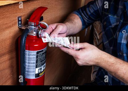 PROSPECT, OREGON – JANUARY 29, 2026: An illustrative editorial photo of a males hands inspecting a red fire extinguisher mounted to a wall to ensure s Stock Photo