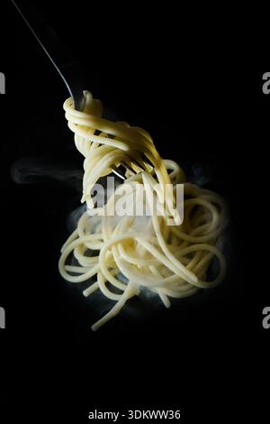Steaming hot spaghetti swirling on a fork against a dark background, representing delicious italian pasta cuisine Stock Photo