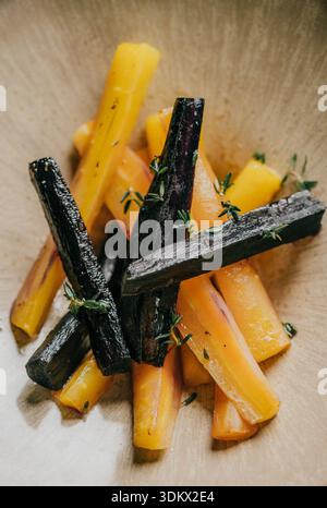 A bowl of carrots with herbs on top. The carrots are cut into different shapes and sizes, and the herbs add a pop of color and flavor to the dish. The Stock Photo