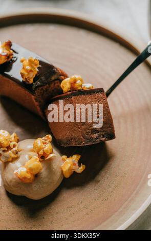 A dessert with a brown plate and a spoon on it. The dessert is a chocolate cake with a caramel sauce and some popcorn on top Stock Photo