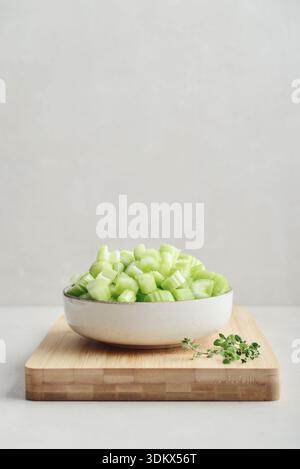 Сhopped stalks of fresh celery in a bowl on bamboo cutting board, closeup Stock Photo