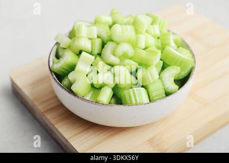 Сhopped stalks of fresh celery in a bowl on bamboo cutting board, closeup Stock Photo