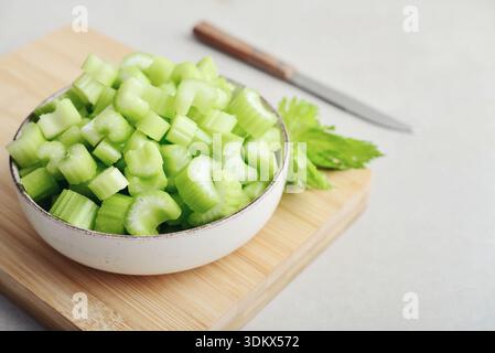 Сhopped stalks of fresh celery in a bowl on bamboo cutting board, closeup Stock Photo