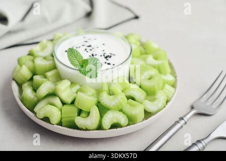 Chopped celery stalks with greek yogurt  in a bowl on bamboo cutting board, closeup Stock Photo