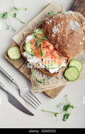 Rye bread sandwich with salted salmon, cucumber, greens and cream cheese on wooden cutting board closeup Stock Photo
