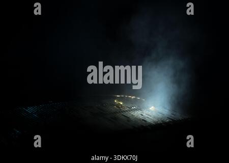 Dramatic night shot of white steam or vapor rising from a metal sewer grate on a dark city street, illuminated by a faint blue light Stock Photo