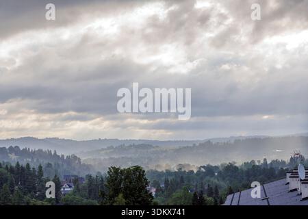 Atmospheric view of a misty valley with distant mountain ridges and a soft glow of sunlight breaking through gray clouds. Stock Photo