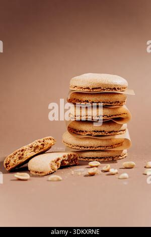 Stacked beige macarons with crumbs and peanuts on brown background copy space Stock Photo
