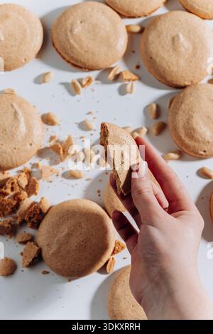 Hand holding bitten peanut macaron on white background with crumbs and nuts Stock Photo
