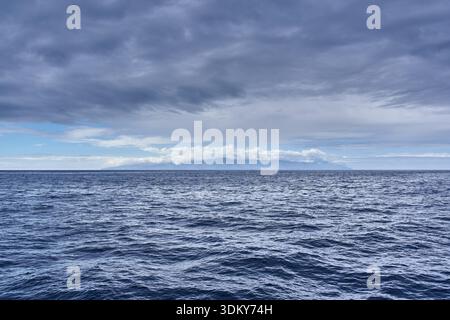 Atlantic Ocean view with distant La Gomera island shrouded in clouds under dramatic gray sky from Tenerife Stock Photo