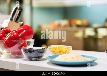 Empty kitchen with pizza ingredients laid out on a kitchen island. Mozzarella, tomatoes and corn placed beside spices and utensils, creating a cozy space for homemade food preparation. Stock Photo