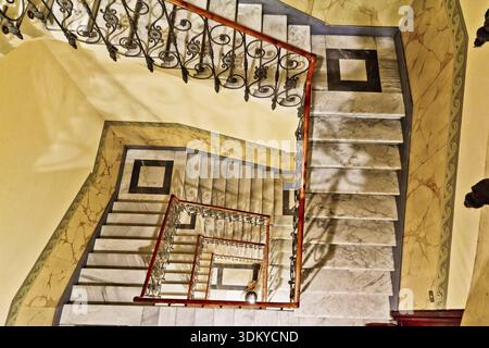 Looking down a winding marble staircase with a metal rail Stock Photo