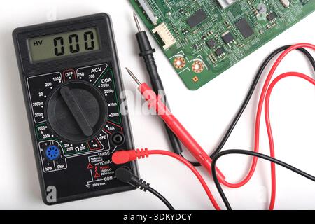Top view digital multimeter with red and black probes and green circuit board on white background. Concept electronics repair and engineering Stock Photo