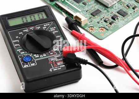 Perspective view digital multimeter next to computer circuit board. Electronic hardware troubleshooting and maintenance concept Stock Photo
