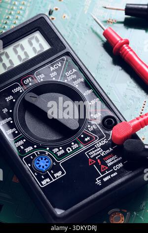 High angle view digital multimeter with connected red and black test leads on green electronic circuit background Stock Photo