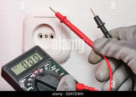 Close up shot technician in protective work gloves using red and black probes to test European electrical socket. Image represents home electrical saf Stock Photo