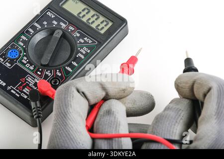 Professional diagnostic tool for measuring voltage, resistance, and current. Hands in grey industrial gloves hold the measurement leads against a neut Stock Photo