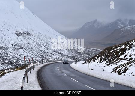 A black car ascends the A93 at Devil's Elbow, Glenshee on the Snow Roads scenic route in Perthshire, Scotland, with snow on the roadside and mountain Stock Photo