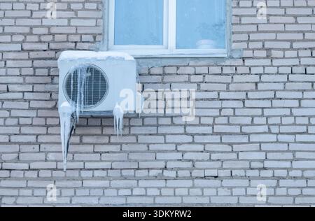 An outdoor air conditioner unit installed on the outer wall of a residential building close-up. Operation of the air conditioner in winter at low temp Stock Photo