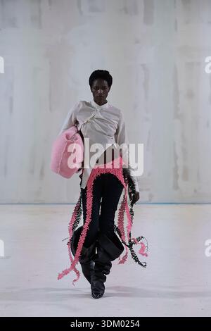 Berlin, Germany, 2nd Feb, 2026. A model walks a minimalist white runway showcasing an avant-garde look during the Kasia Kucharska Autumn/Winter 2026 (AW26) presentation. The outfit features a draped white long-sleeve blouse with a high asymmetric hemline, paired with low-rise black trousers. A bright pink, textured woven loincloth-style overlay sits at the hips, trailing into long dangling fringe panels. The look is accessorized with an oversized plush pink bag held under one arm and chunky black slouchy boots, set against a raw industrial studio wall. Credit: Felix Wolf/Ģ����ý Live News Stock Photo