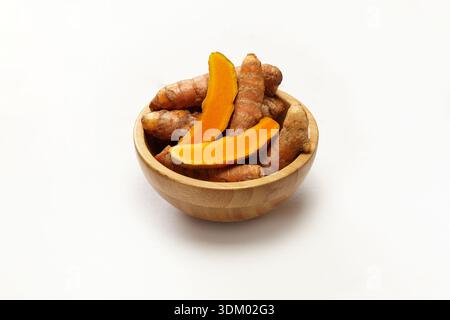 Fresh turmeric roots and sliced turmeric arranged in a small wooden bowl on clean white background, highlighting natural colour, texture, and herbal Stock Photo