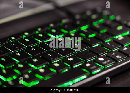 Close up of a laptop keyboard with green backlit keys, technology concept, programming, cybersecurity, gaming Stock Photo
