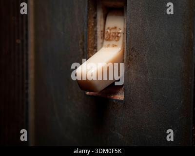 Macro close-up of a vintage cream-colored toggle light switch in the off position, set against a dark, weathered wall plate with visible grime and tex Stock Photo