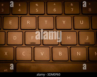 Macro top-down view of a QWERTY laptop keyboard with black keys and white lettering under warm, atmospheric lighting. Stock Photo
