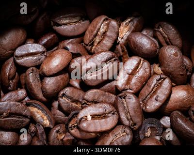 Top-down macro close-up of a pile of whole roasted coffee beans, showcasing detailed oily textures and rich brown tones. Stock Photo