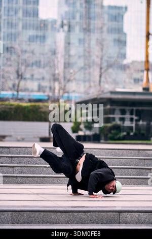 Young adult man energetically break dancing and doing handstands outside some office buildings, wearing comfortable clothes, with lots of attitude, Stock Photo