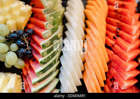 Colorful sliced fruit platter with watermelon melon grapes pineapple arranged in neat rows for fresh buffet presentation Stock Photo