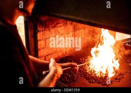 Blacksmith working at a glowing forge, heating iron in open flames, showcasing traditional metalworking, craftsmanship and intense fire light Stock Photo