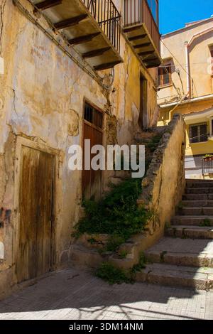 A narrow stepped street in Monreale, Sicily, Italy. An abandoned vernacular 18th-19th century building on the left features balconies with black rails Stock Photo