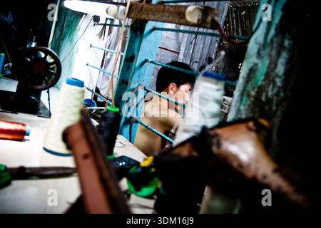 Shoemakers working by hand in a small workshop in Hoi An, Vietnam, crafting and repairing footwear using traditional manual techniques Stock Photo