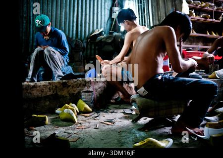 Shoemakers working by hand in a small workshop in Hoi An, Vietnam, crafting and repairing footwear using traditional manual techniques Stock Photo