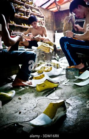 Shoemakers working by hand in a small workshop in Hoi An, Vietnam, crafting and repairing footwear using traditional manual techniques Stock Photo
