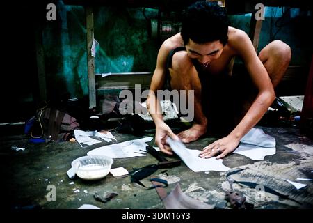 Shoemakers working by hand in a small workshop in Hoi An, Vietnam, crafting and repairing footwear using traditional manual techniques Stock Photo