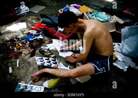 Shoemakers working by hand in a small workshop in Hoi An, Vietnam, crafting and repairing footwear using traditional manual techniques Stock Photo