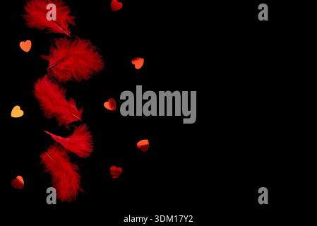 Red feathers and red shiny hearts on a black background. Stock Photo